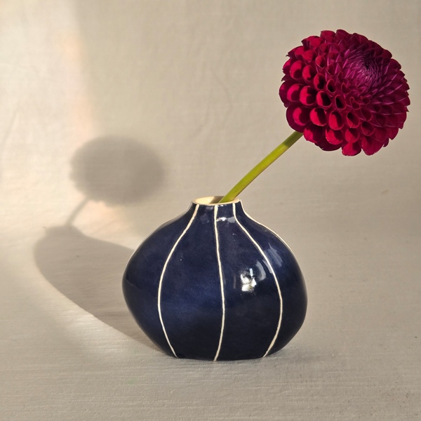 small round dark blue ceramic bud vase with flower